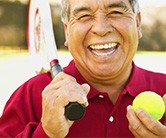 Close up of an older man laughing holding tennis racquet and ball